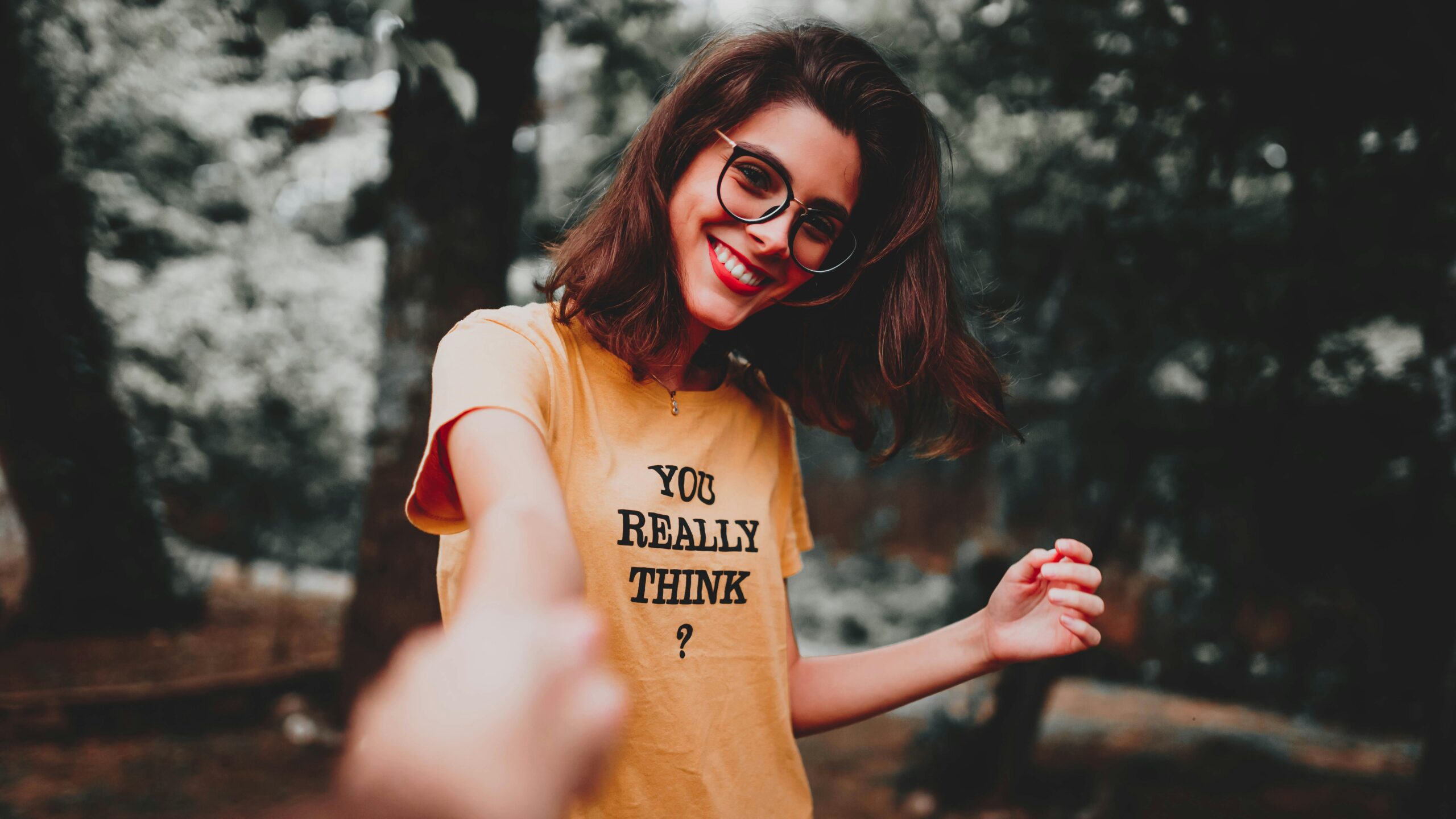 Cheerful woman in glasses holding hands outdoors, wearing a text t-shirt.