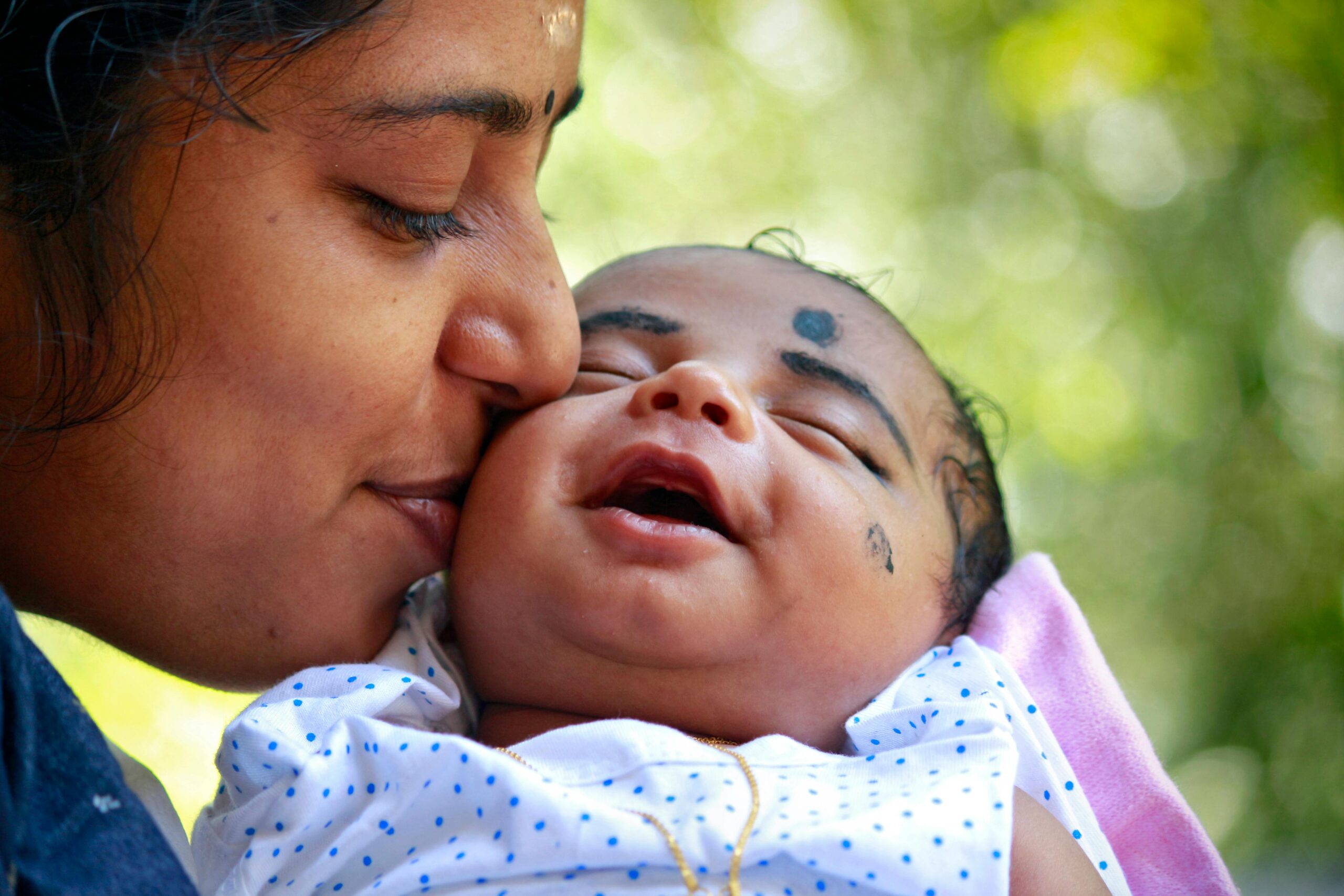 Heartwarming portrait of a mother kissing her smiling baby outdoors.