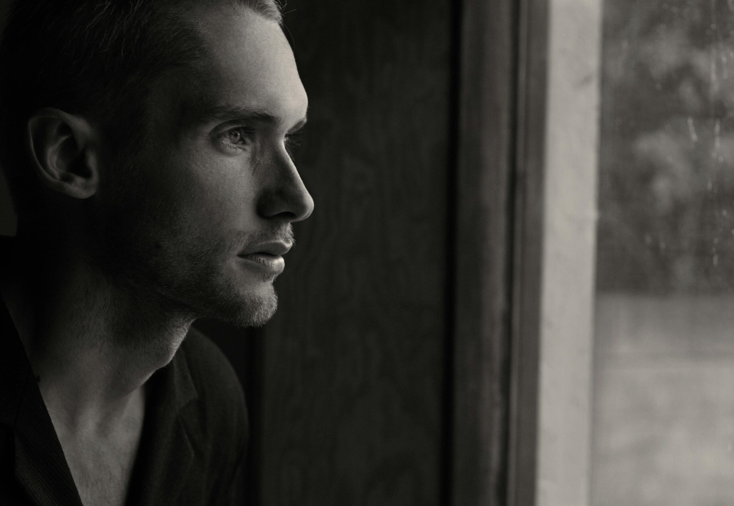 Side profile portrait of a man gazing out a window in black and white.