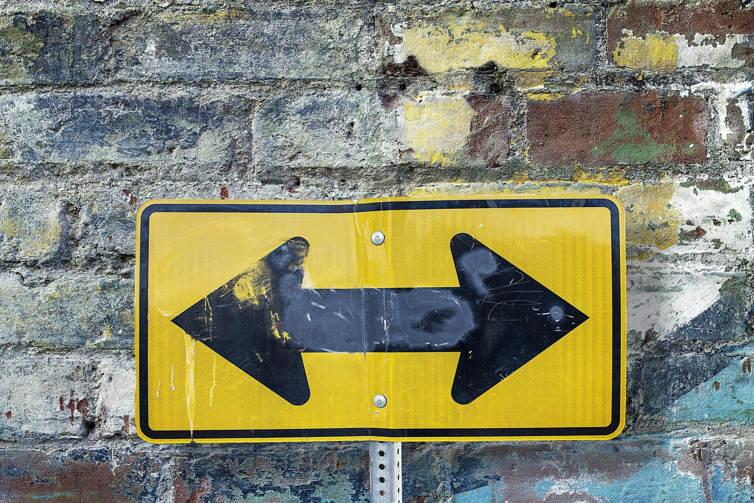 Weathered yellow two-way street sign on a textured rustic brick wall. Urban art style.