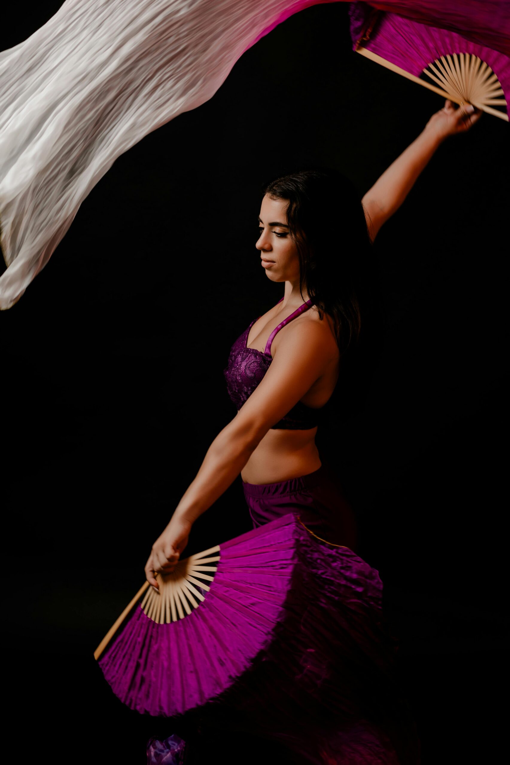 A graceful woman performs a dance with vibrant fans, showcasing fluid motion and elegance.