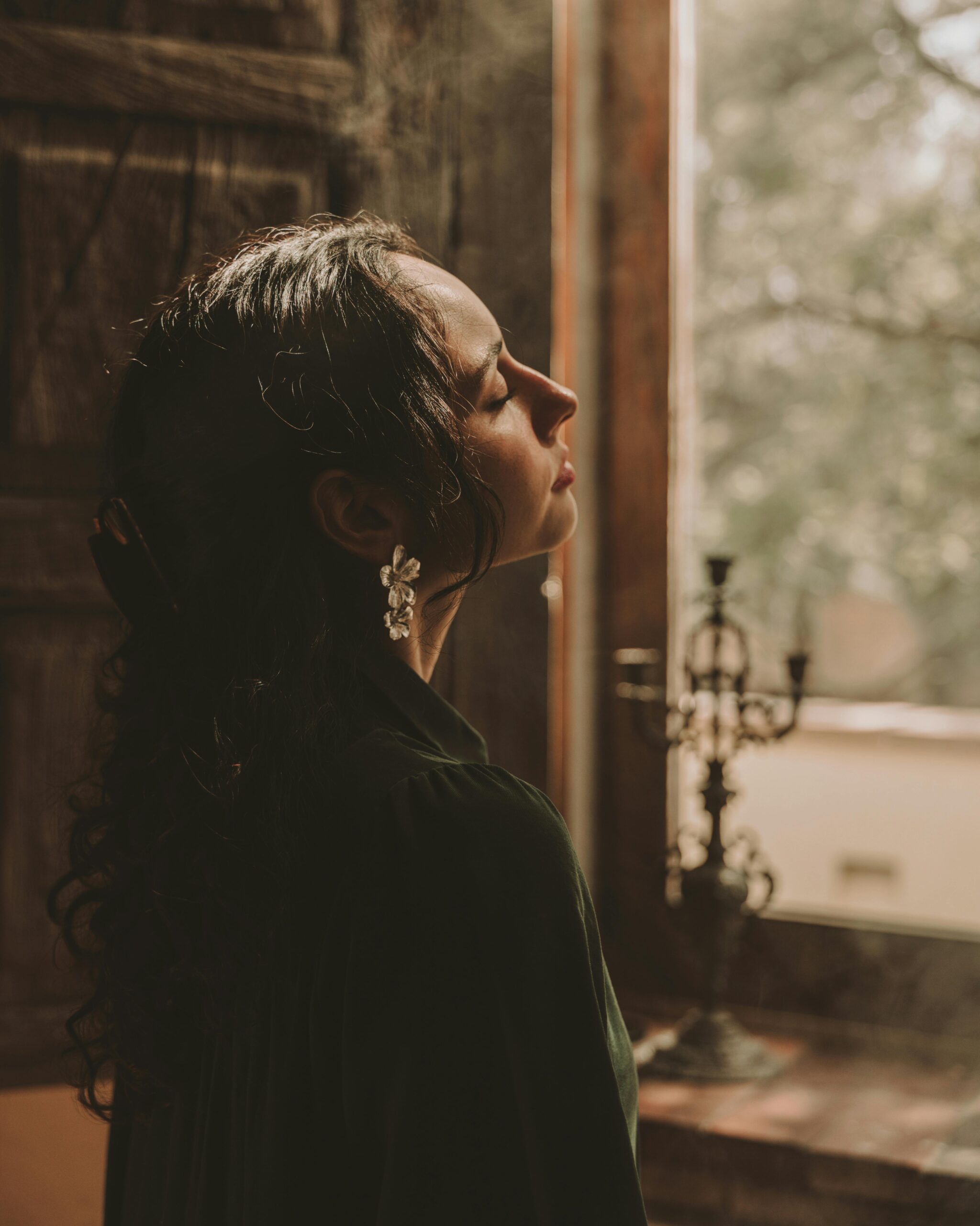 A contemplative woman in a vintage room, softly lit by natural light.