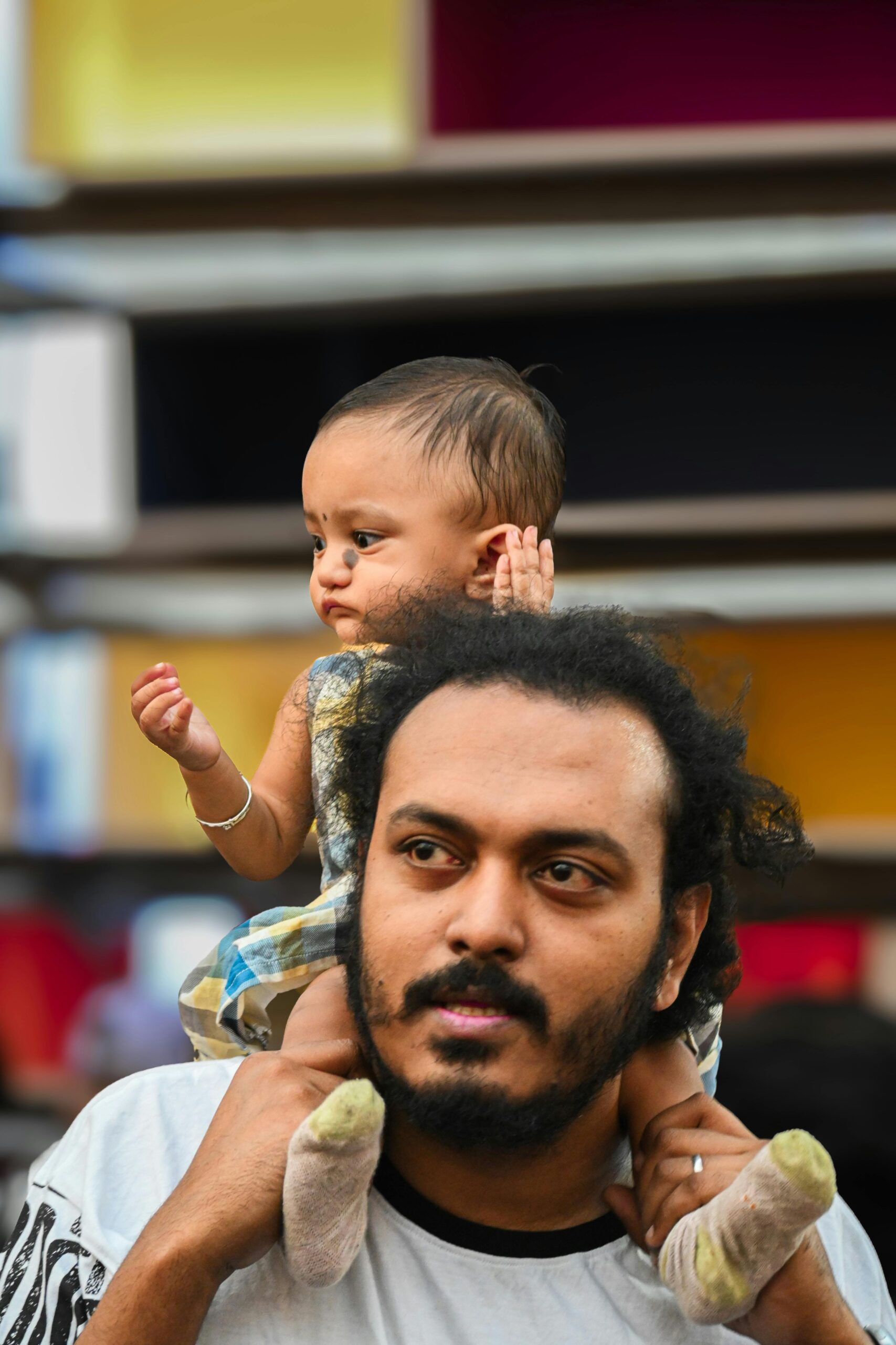 A father carrying his baby on his shoulders in a busy Kolkata street. Captured outside, showcasing urban life.