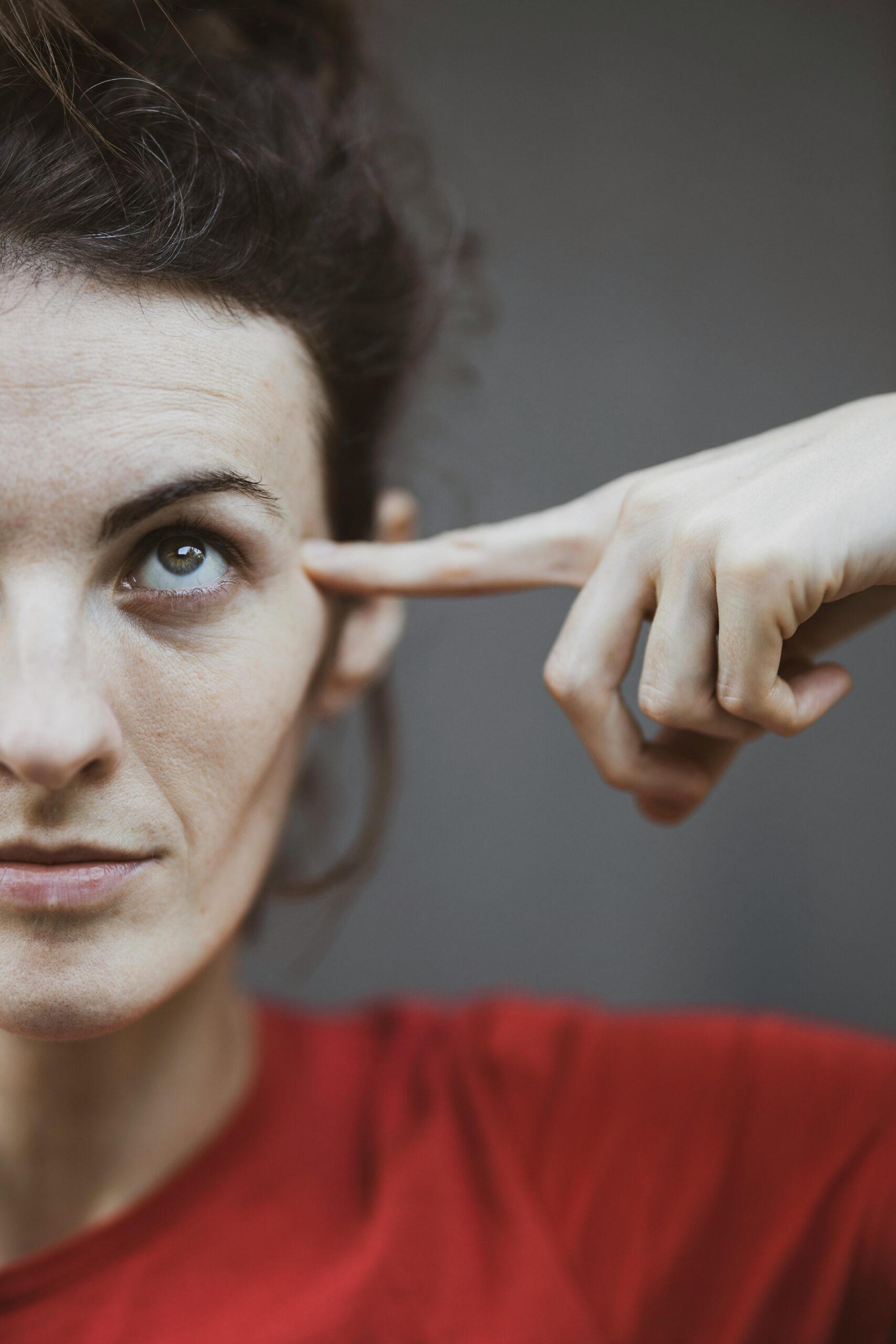 Close-up portrait of a woman in red, pointing to her temple, capturing a thoughtful expression.