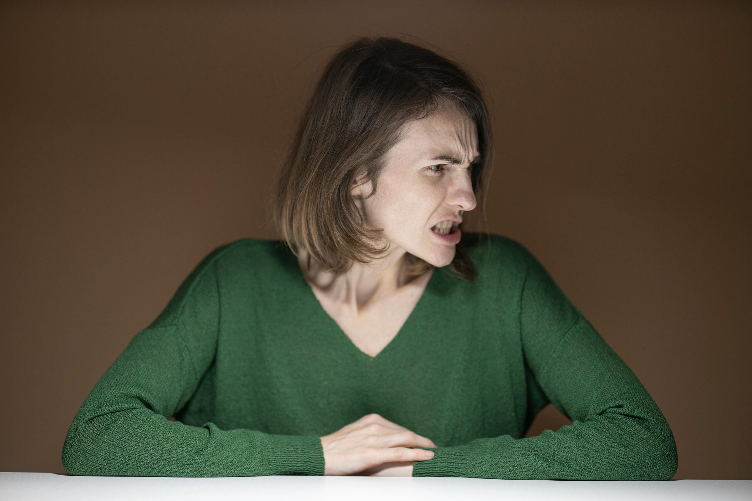 Portrait of an angry woman in a green sweater sitting indoors, looking sideways.