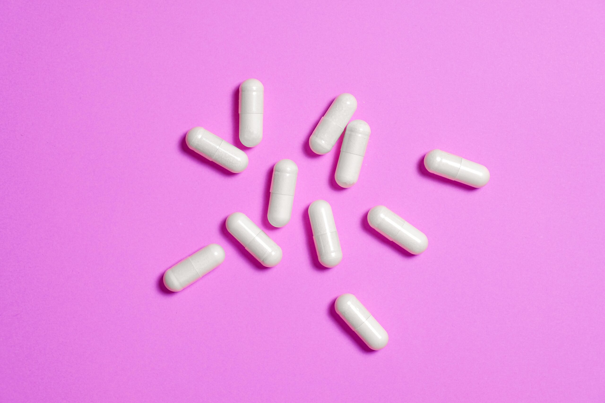 White medicine capsules scattered on vibrant pink background, highlighting modern pharmaceutical design.