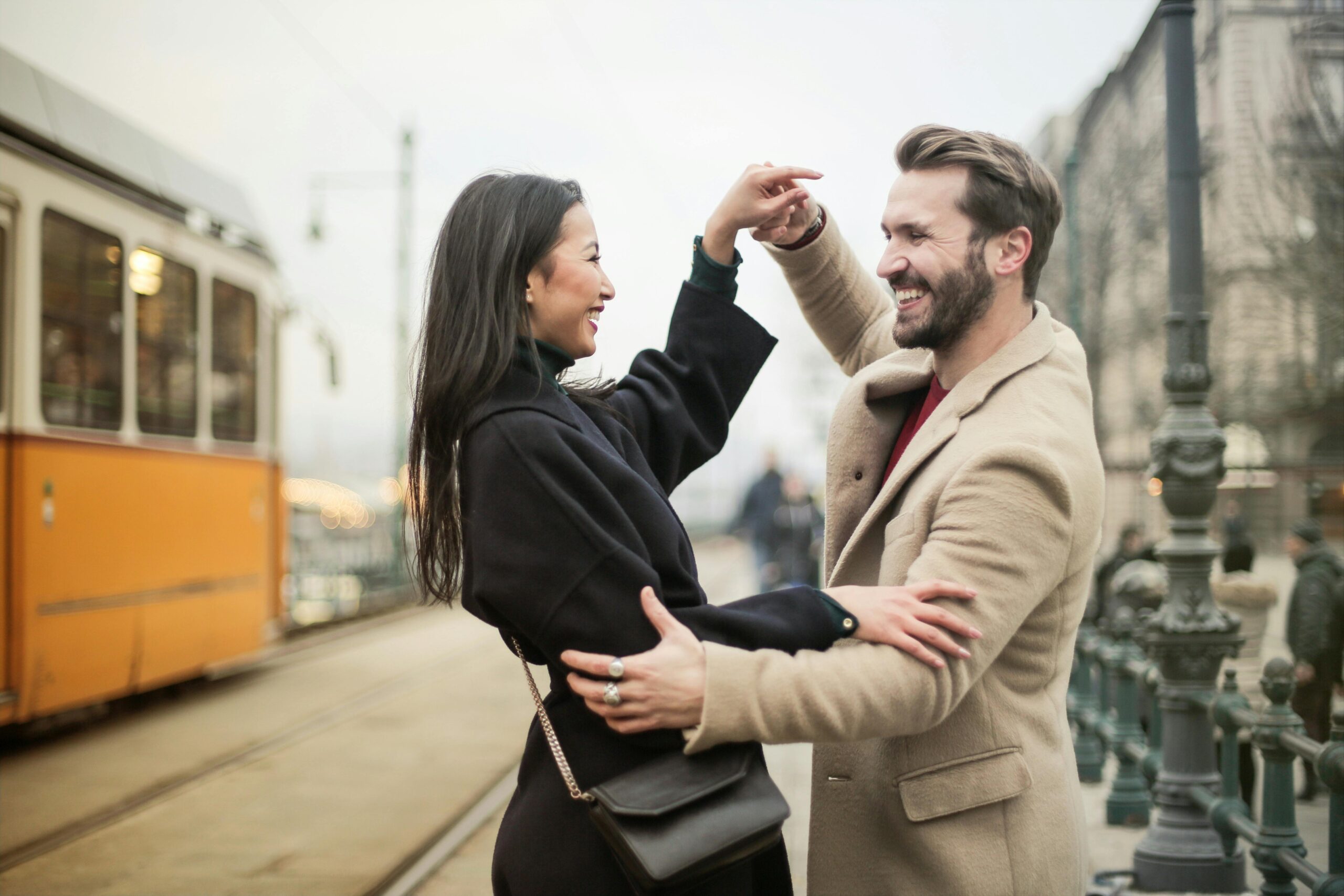 Joyful couple dances on a tram-lined city street, sharing laughter and happiness.