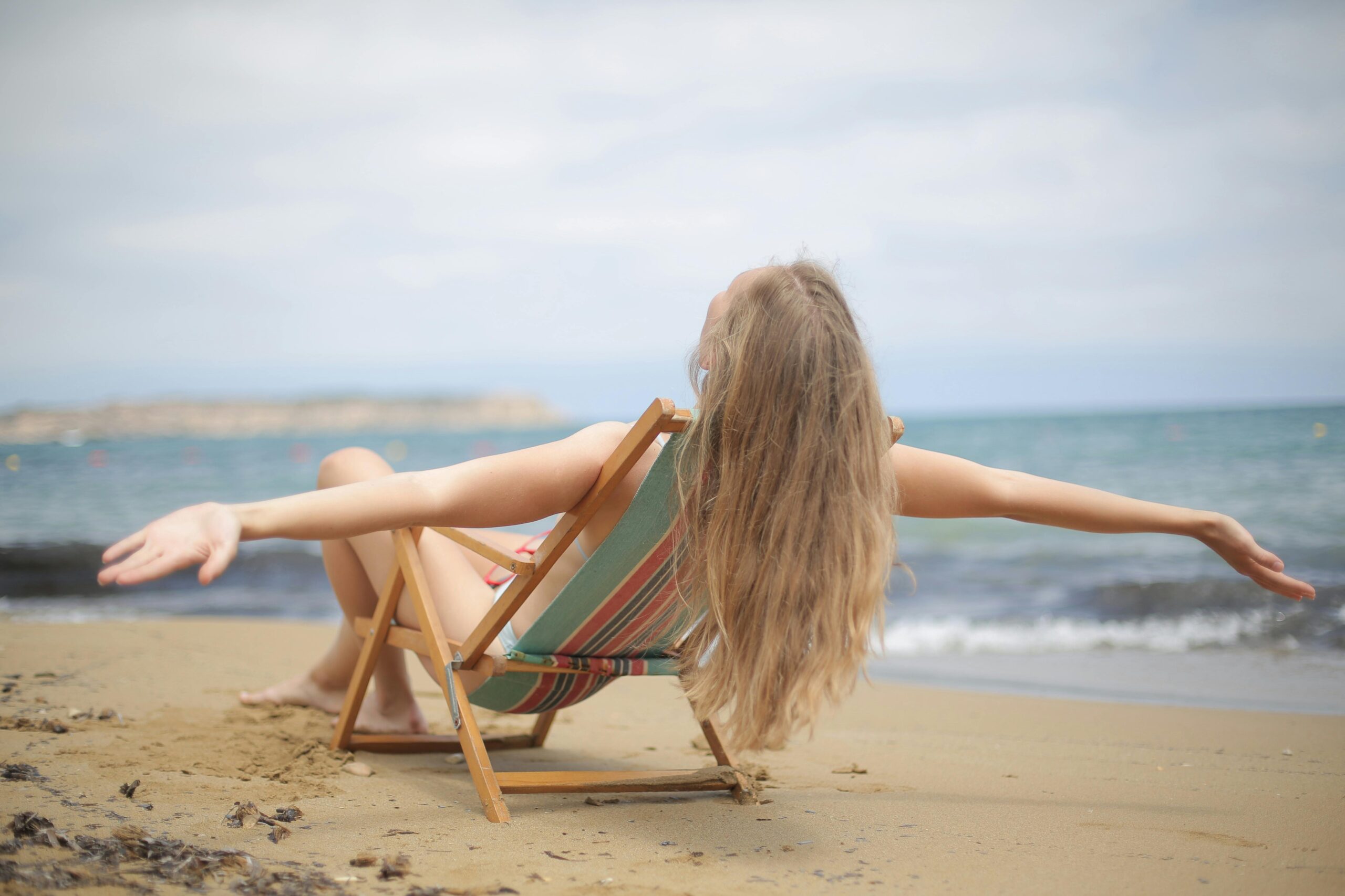 A woman enjoys a relaxing moment on a sandy beach, arms outstretched, embracing the summer vibes.