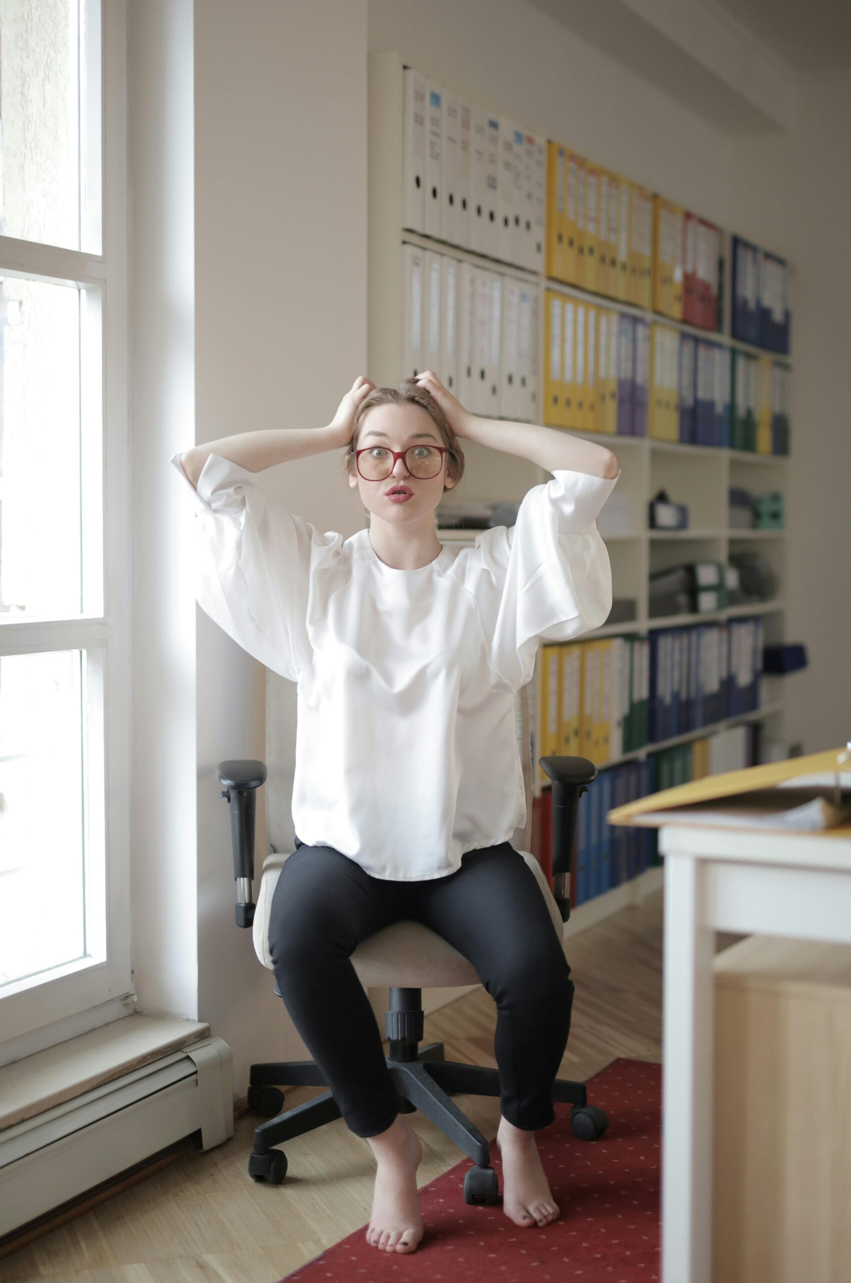 Woman in a modern office expressing frustration while seated in front of a stack of binders.