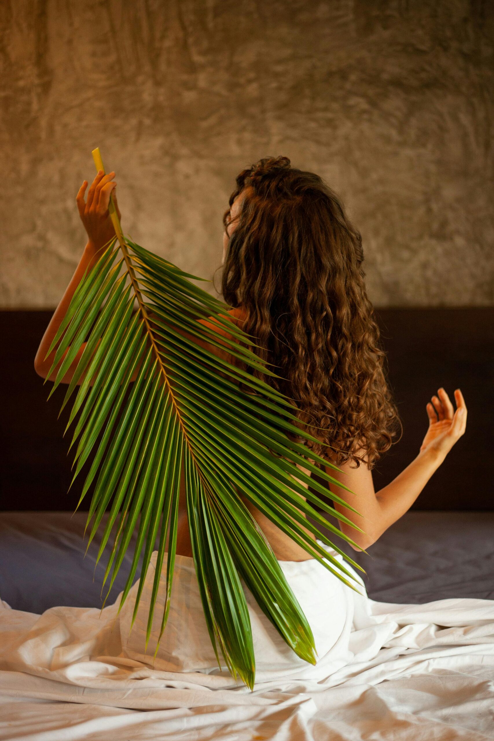 Back view of a woman with a palm leaf adds a tropical and serene vibe.