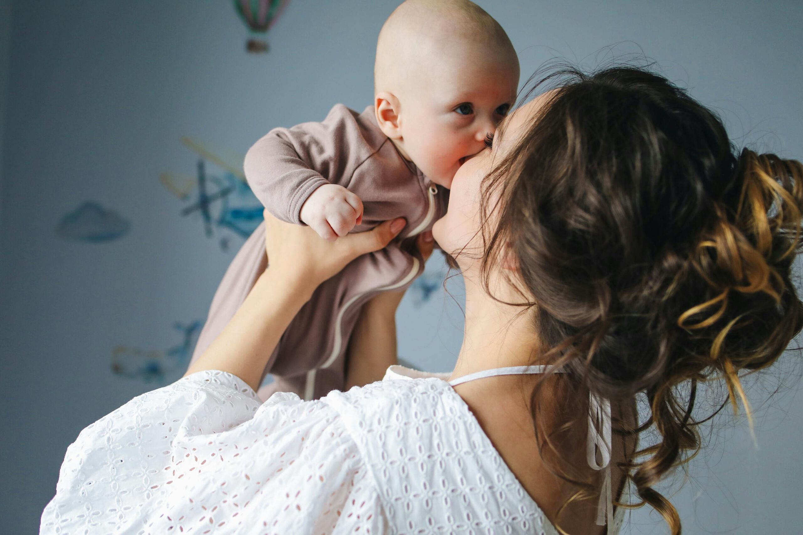 A heartwarming scene of a mother lovingly kissing her baby in a decorated room.