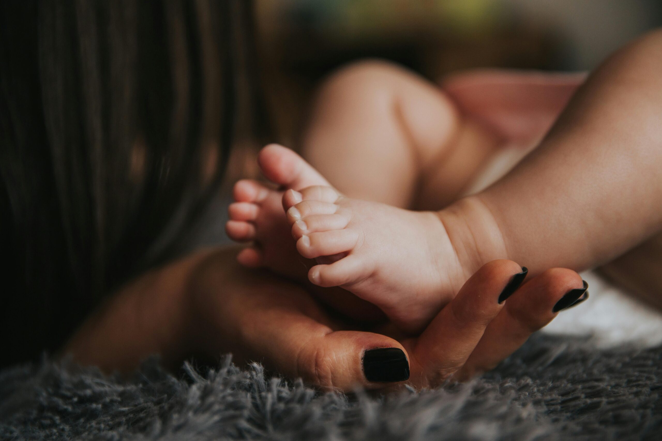 Close-up of a mother's hand gently holding her baby's tiny feet, symbolizing warmth and affection.