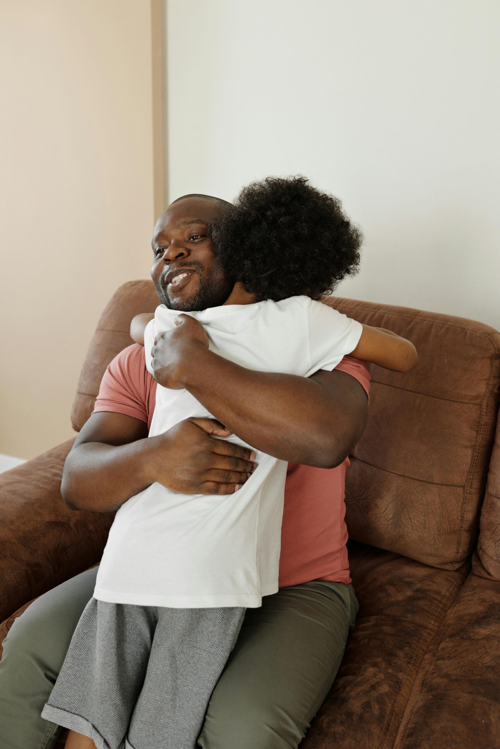 A father warmly embraces his young son on a sofa, capturing a moment of affection and togetherness.