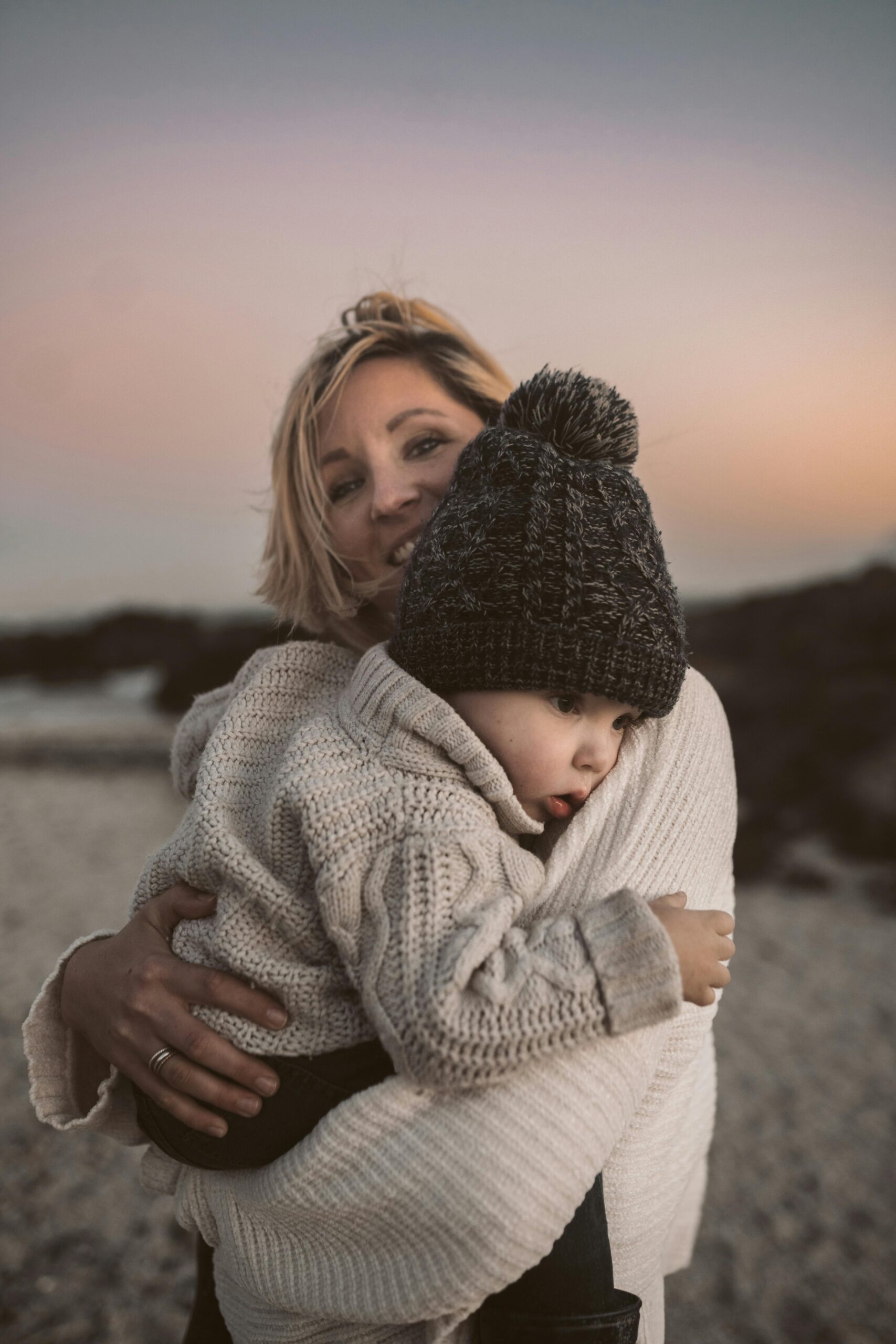 Heartwarming portrait of a mother and child wrapped in cozy winter sweaters, embracing at sunset.