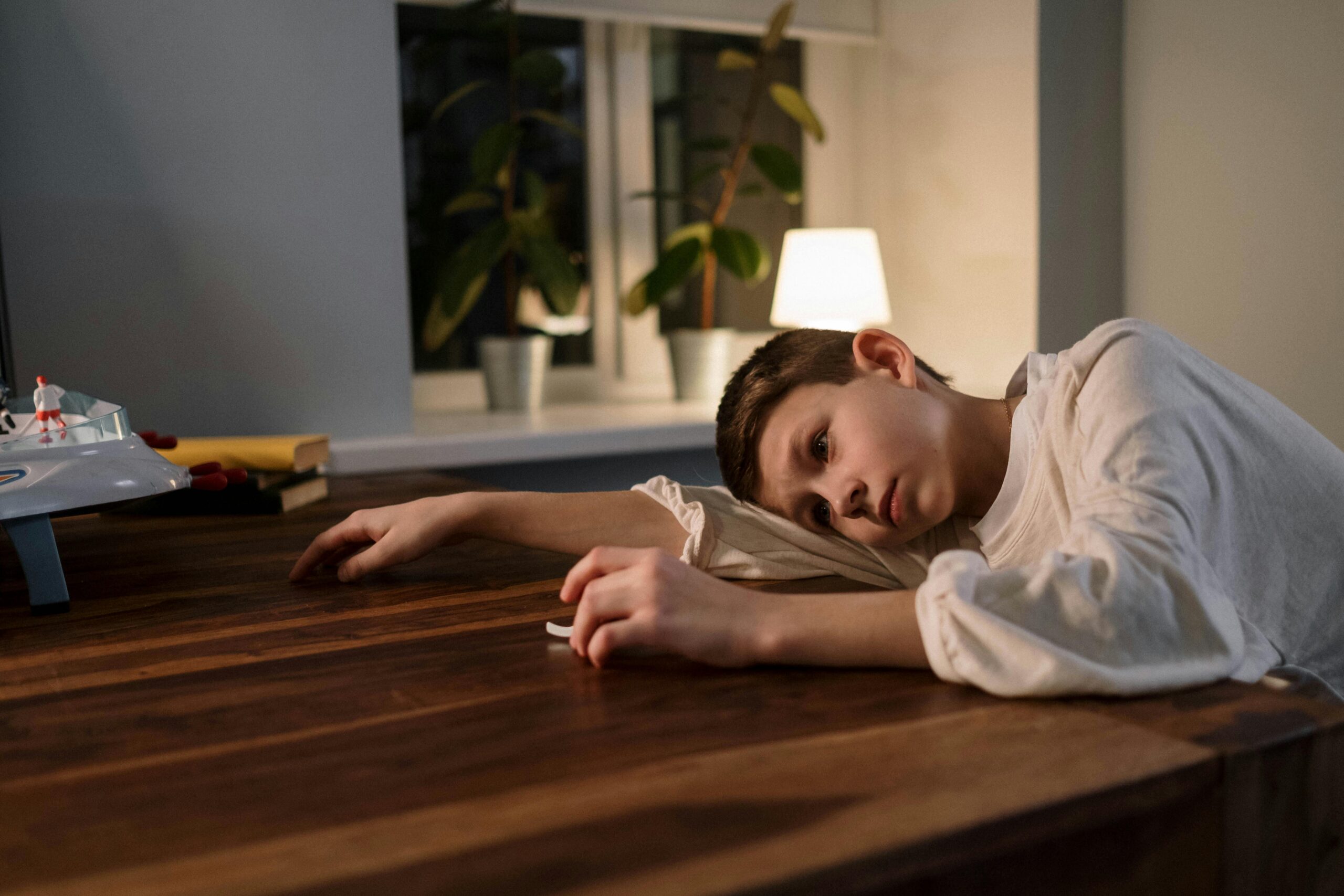 A young boy in thoughtful pose at a table, reflecting emotions indoors.