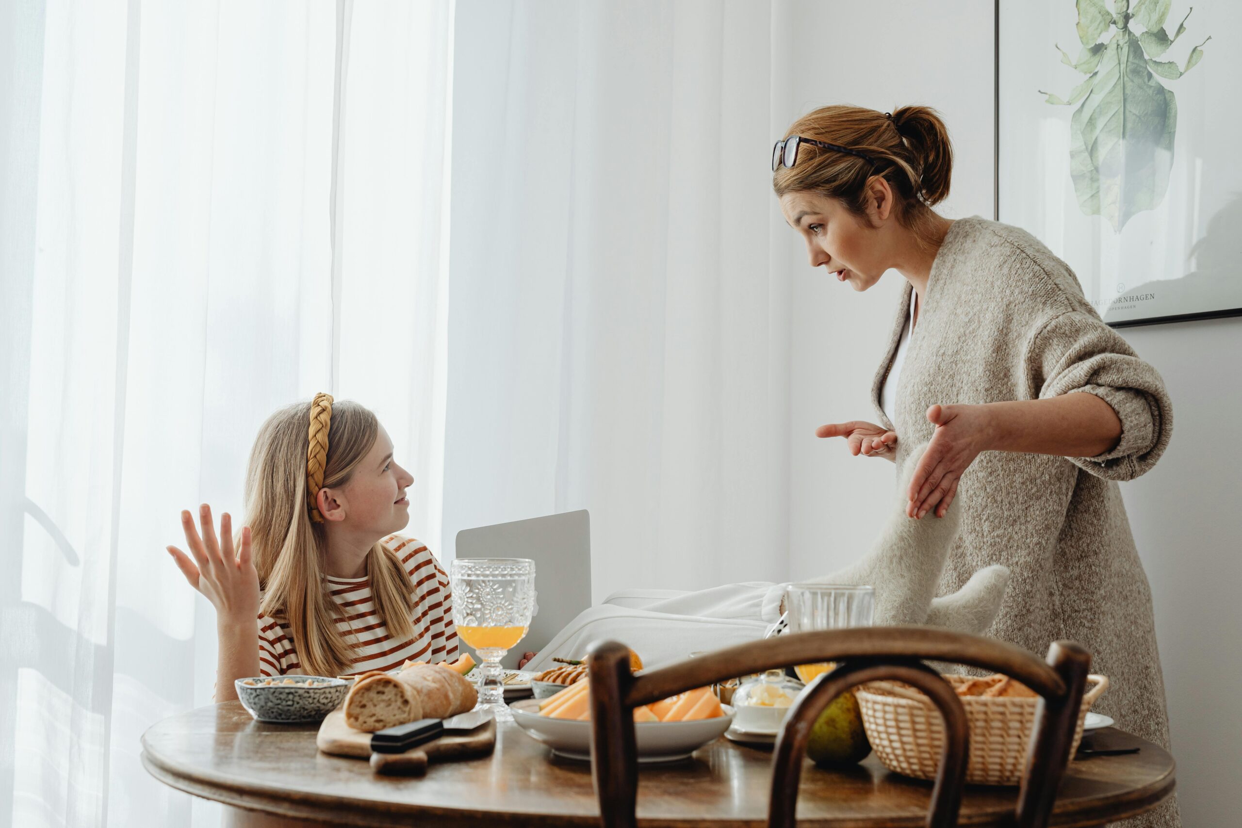 A mother and teenage daughter having a discussion while having breakfast at home.