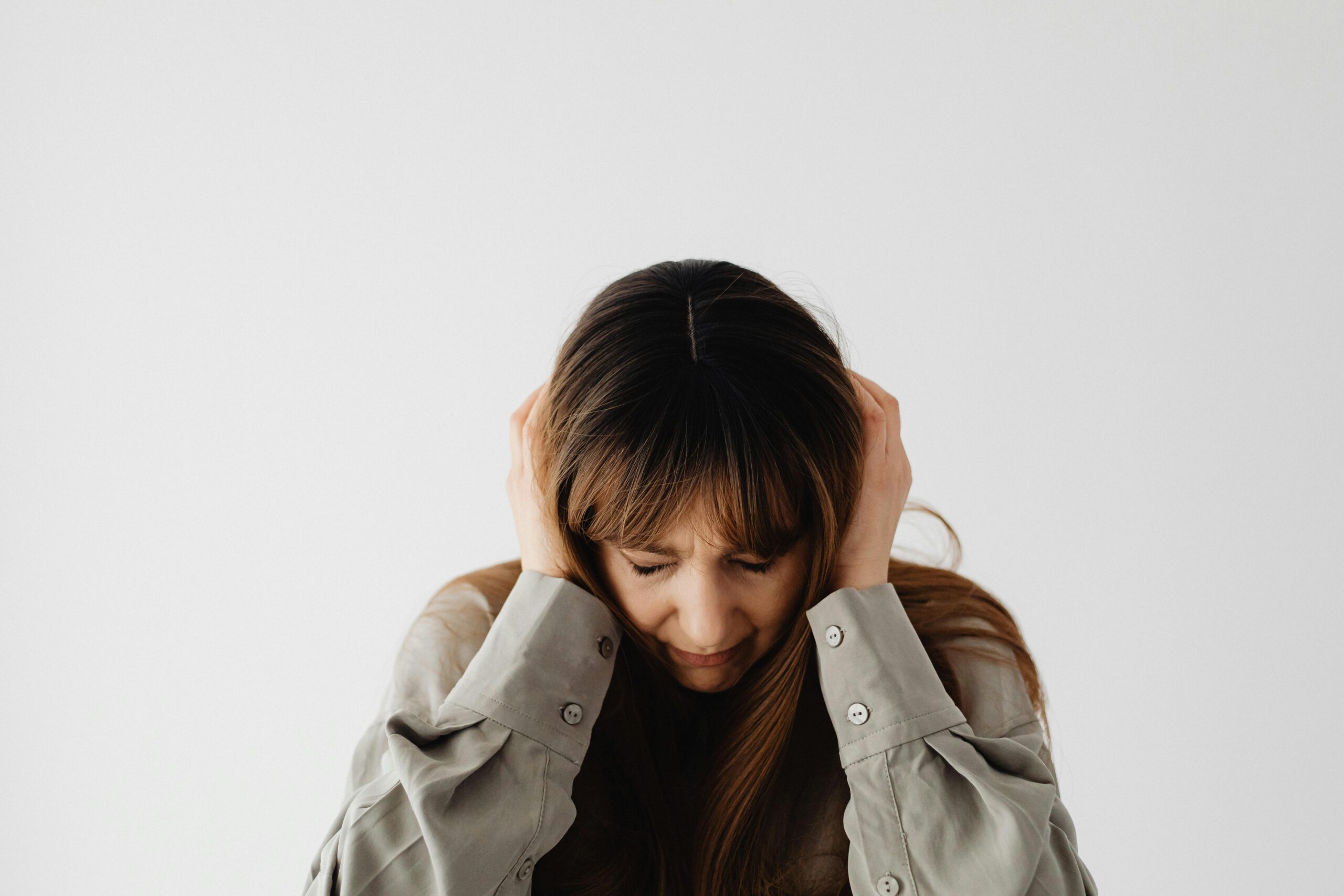 Woman with closed eyes holding head, conveying stress and emotions against a plain white background.