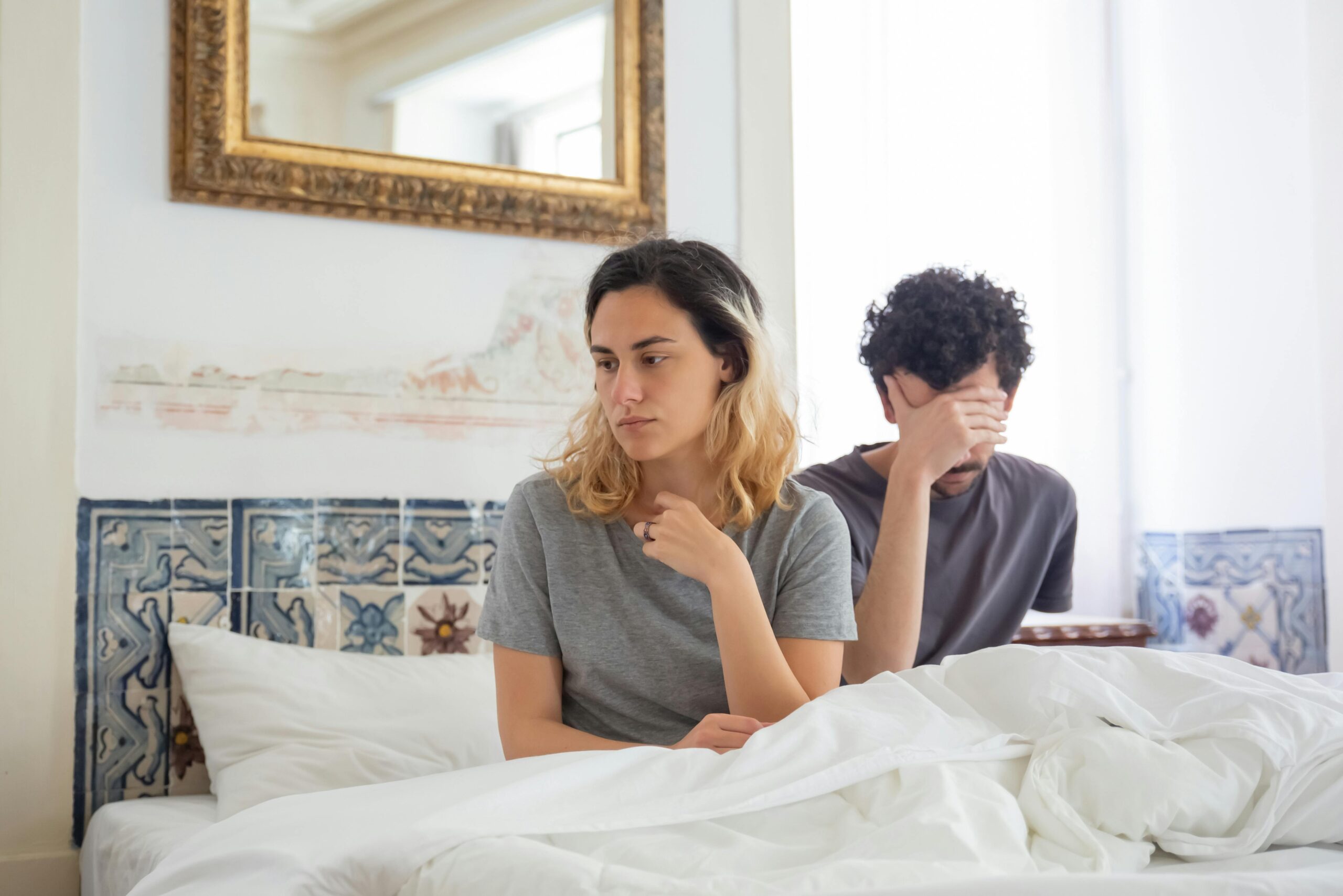 A couple sits together in a bedroom, experiencing a moment of misunderstanding.