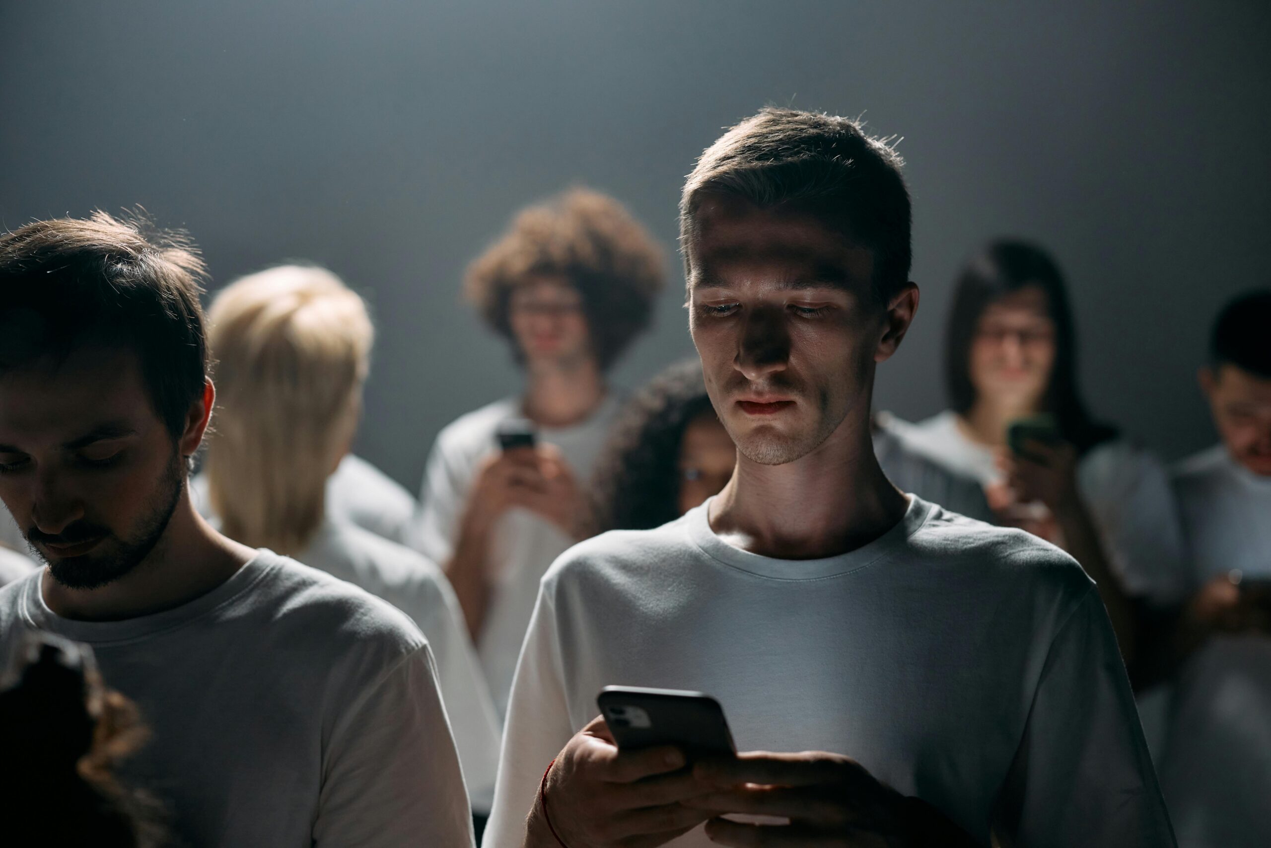 A diverse group of people focused on their smartphones in a dimly lit setting, highlighting social isolation.