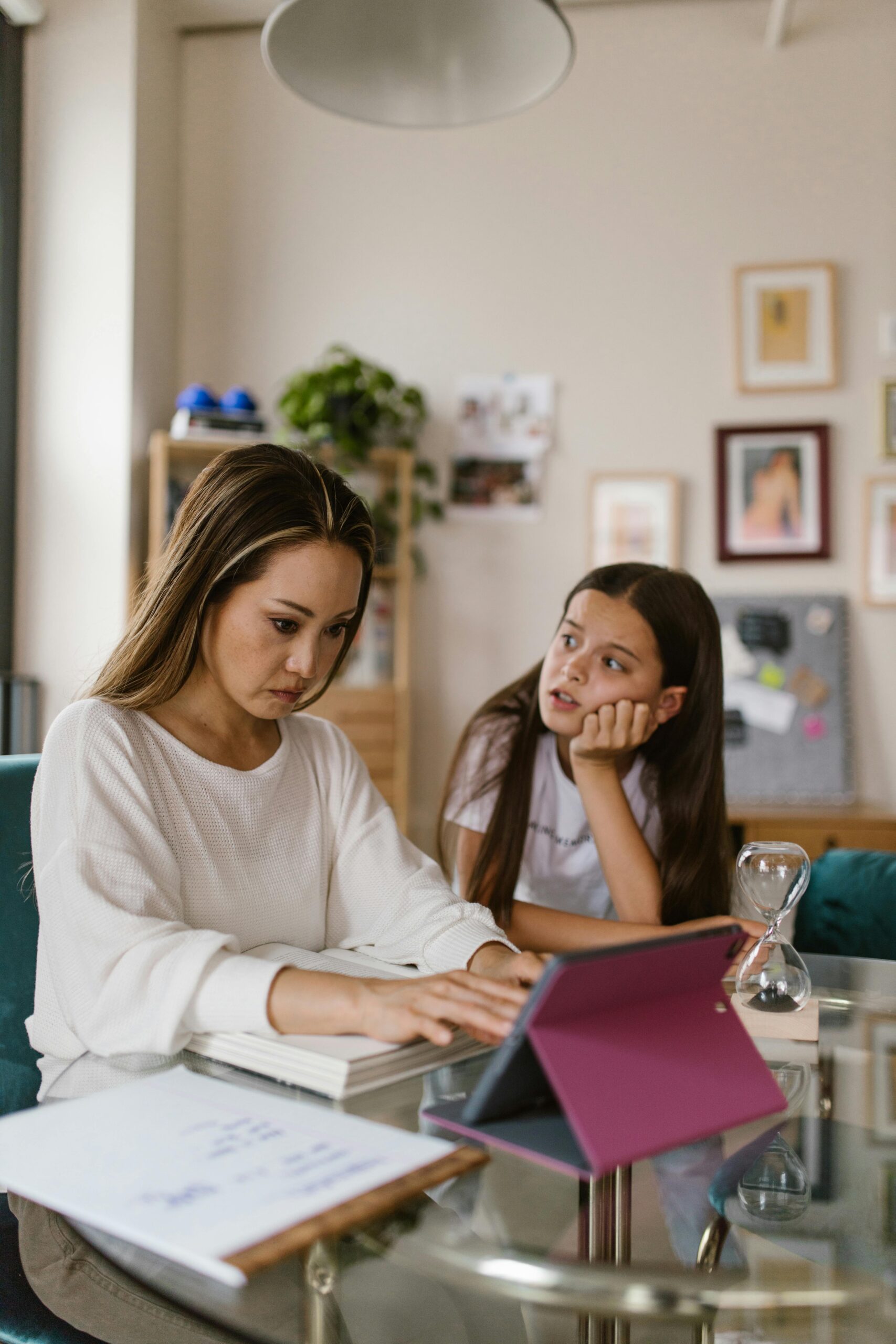 Woman focused on tablet work while child looks on, in a home office environment.