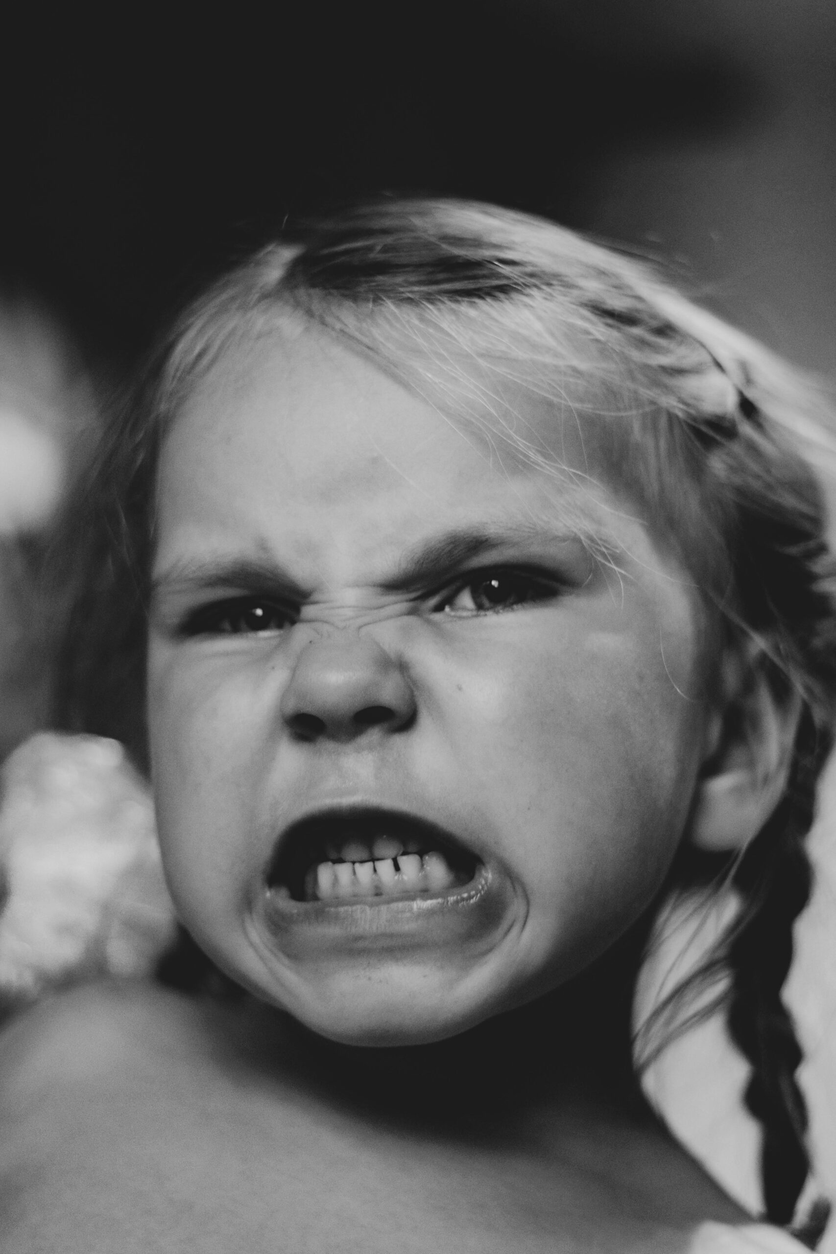 Black and white portrait of a young girl displaying a fierce facial expression, creating a dramatic mood.