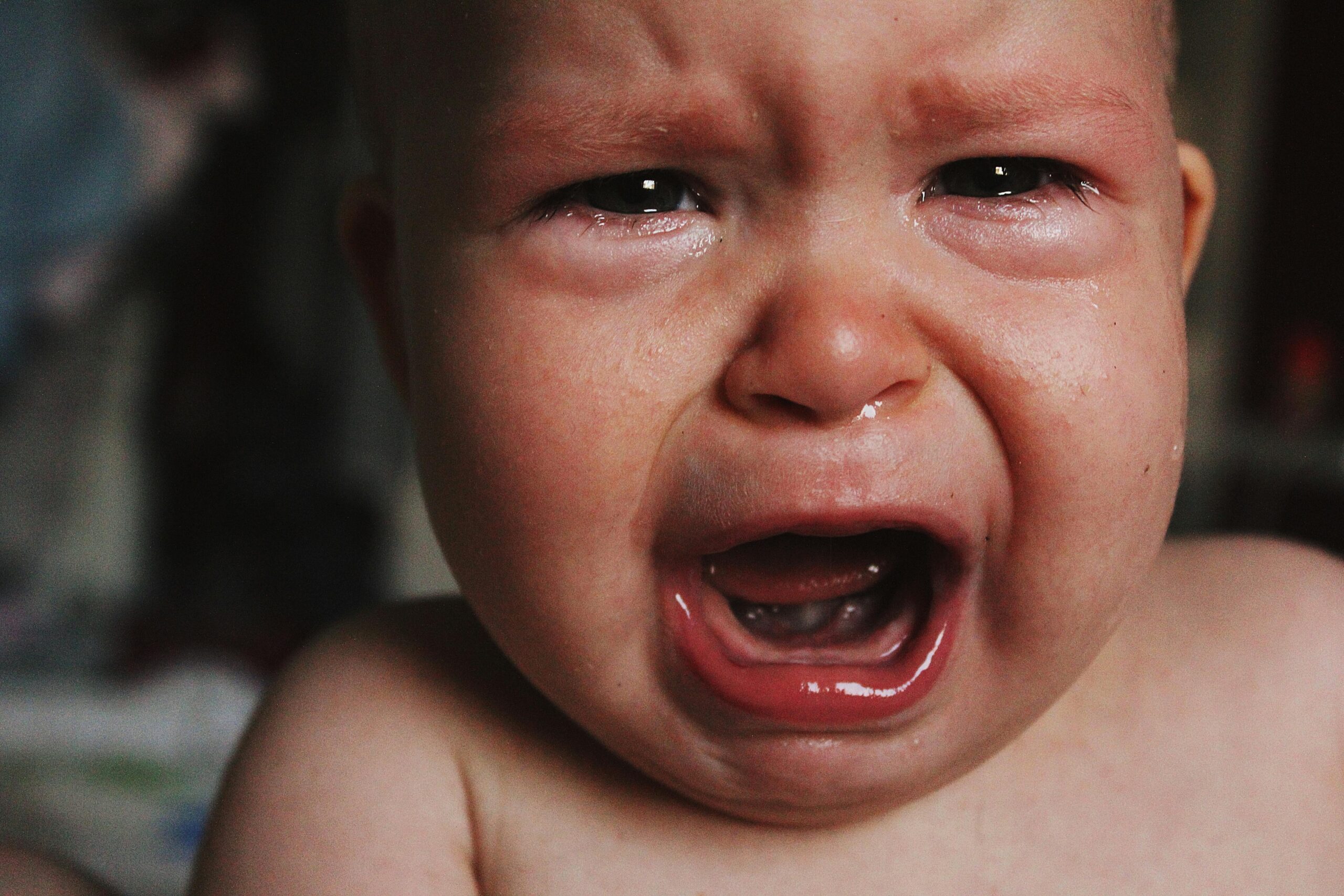 A close-up portrait of a crying baby, capturing raw emotion and sadness with tears visible on the cheeks.