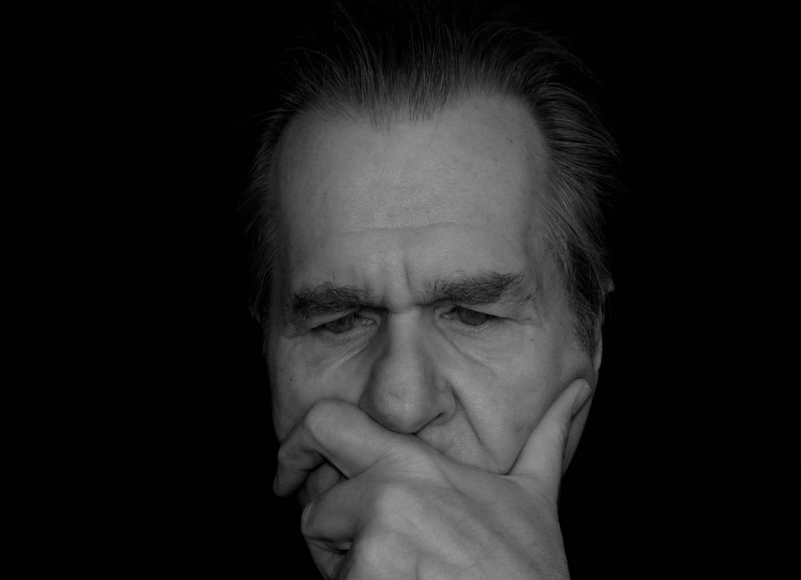 Close-up portrait of a thoughtful elderly man against a dark background.