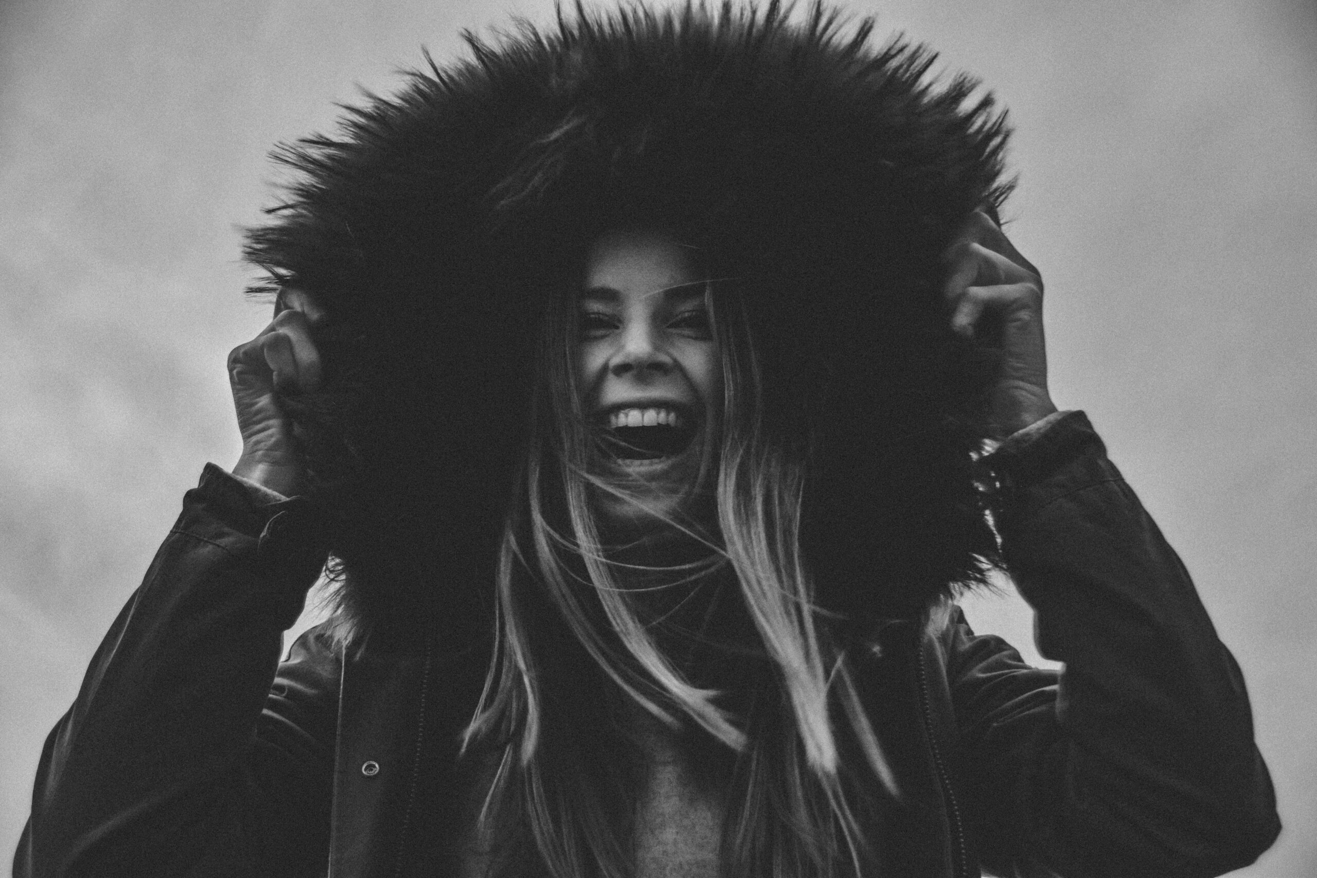 Black and white portrait of a joyful woman in a fur hood, radiating happiness.