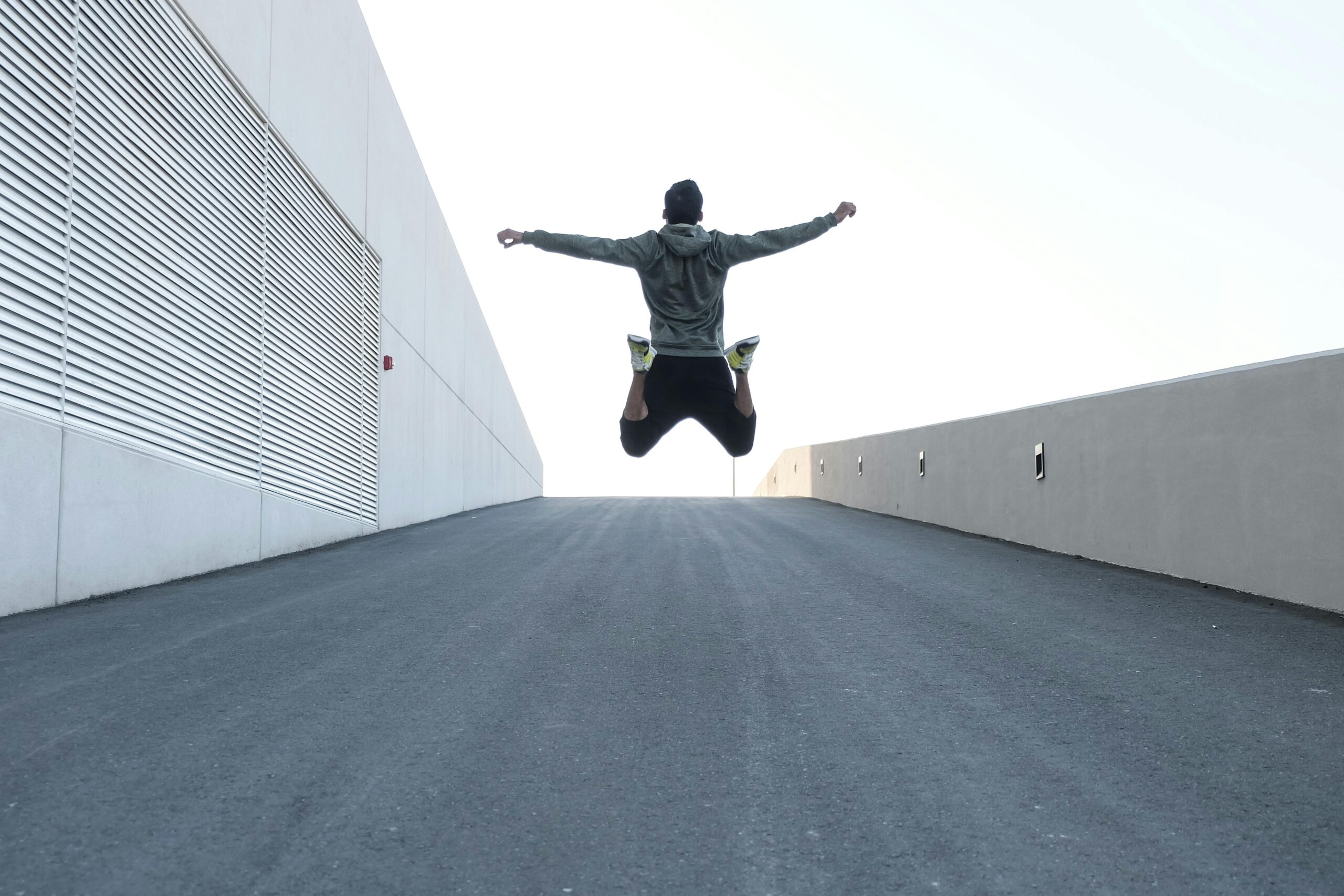 Man jumping on urban road with arms spread wide in Dubai, showcasing freedom and energy.