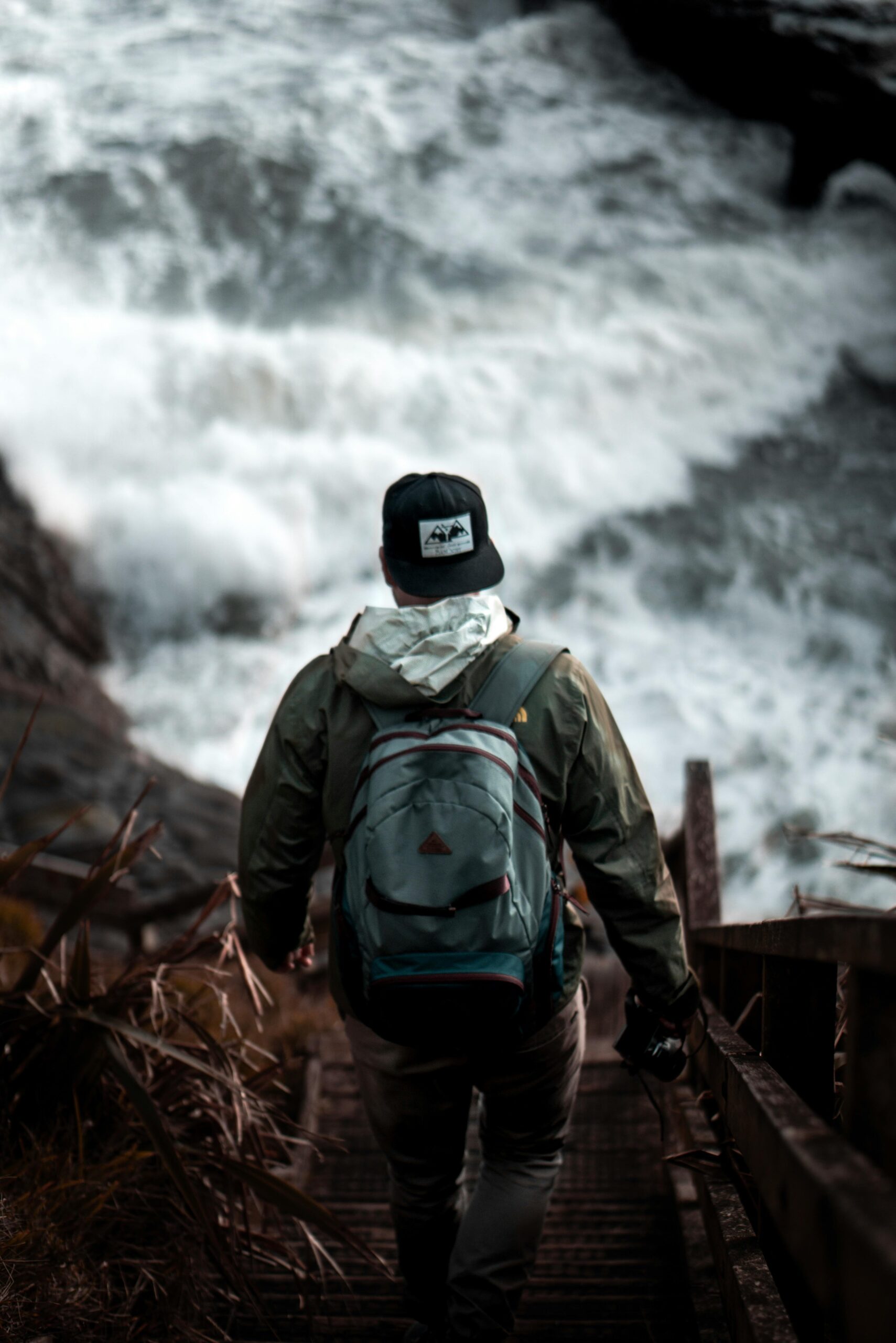 Traveler with backpack walks down staircase towards the ocean in Muriwai, New Zealand.