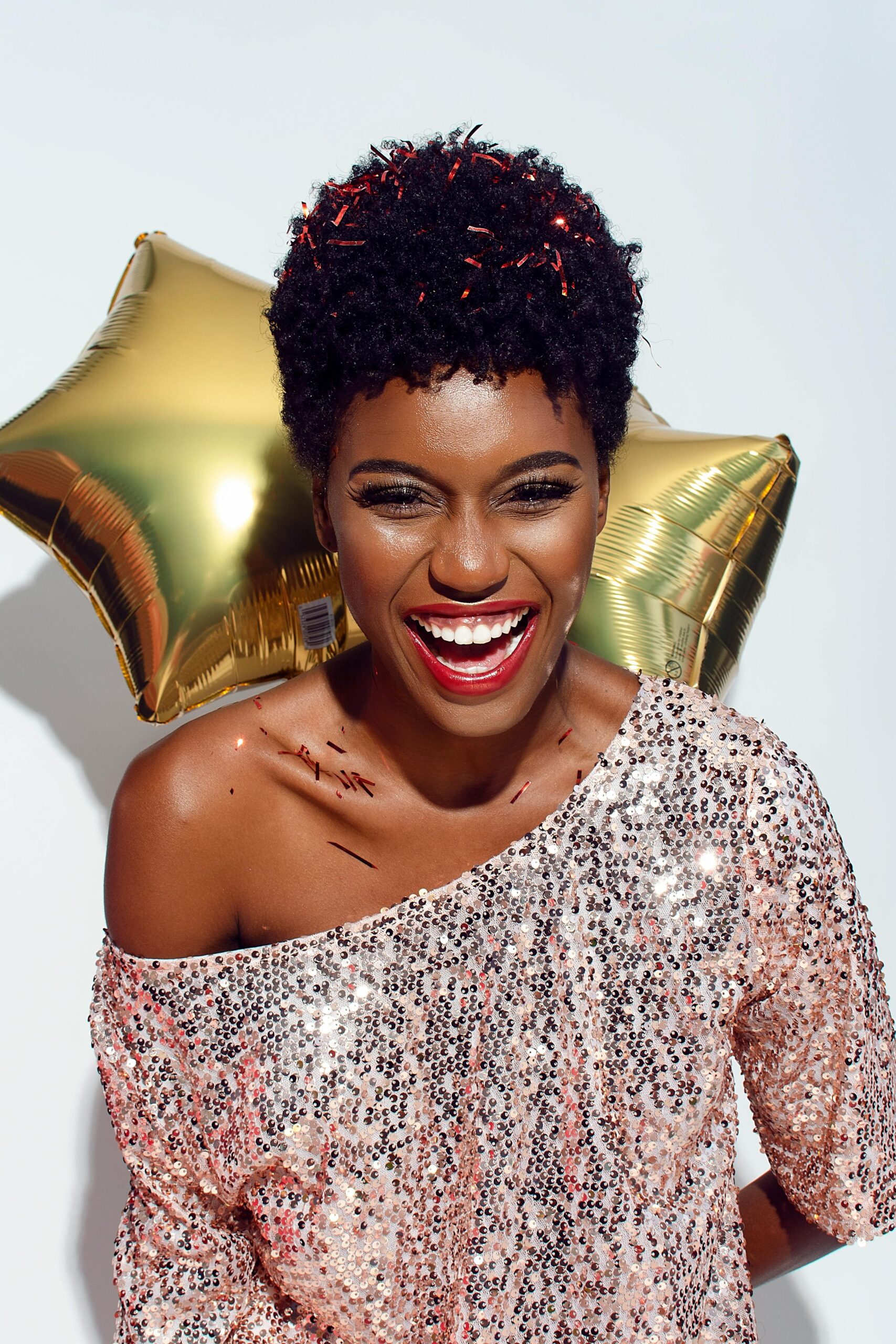 A joyful woman celebrates New Year's with a smile, confetti, and balloons.