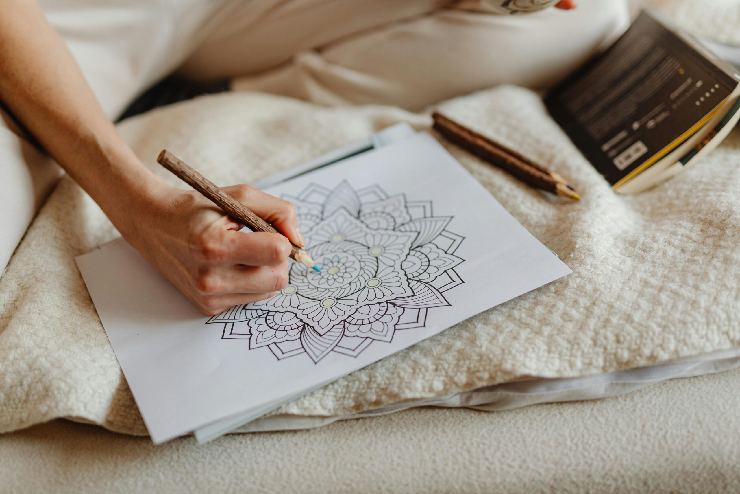 Person uses a brown pencil to color a mandala drawing on paper, creating art indoors.