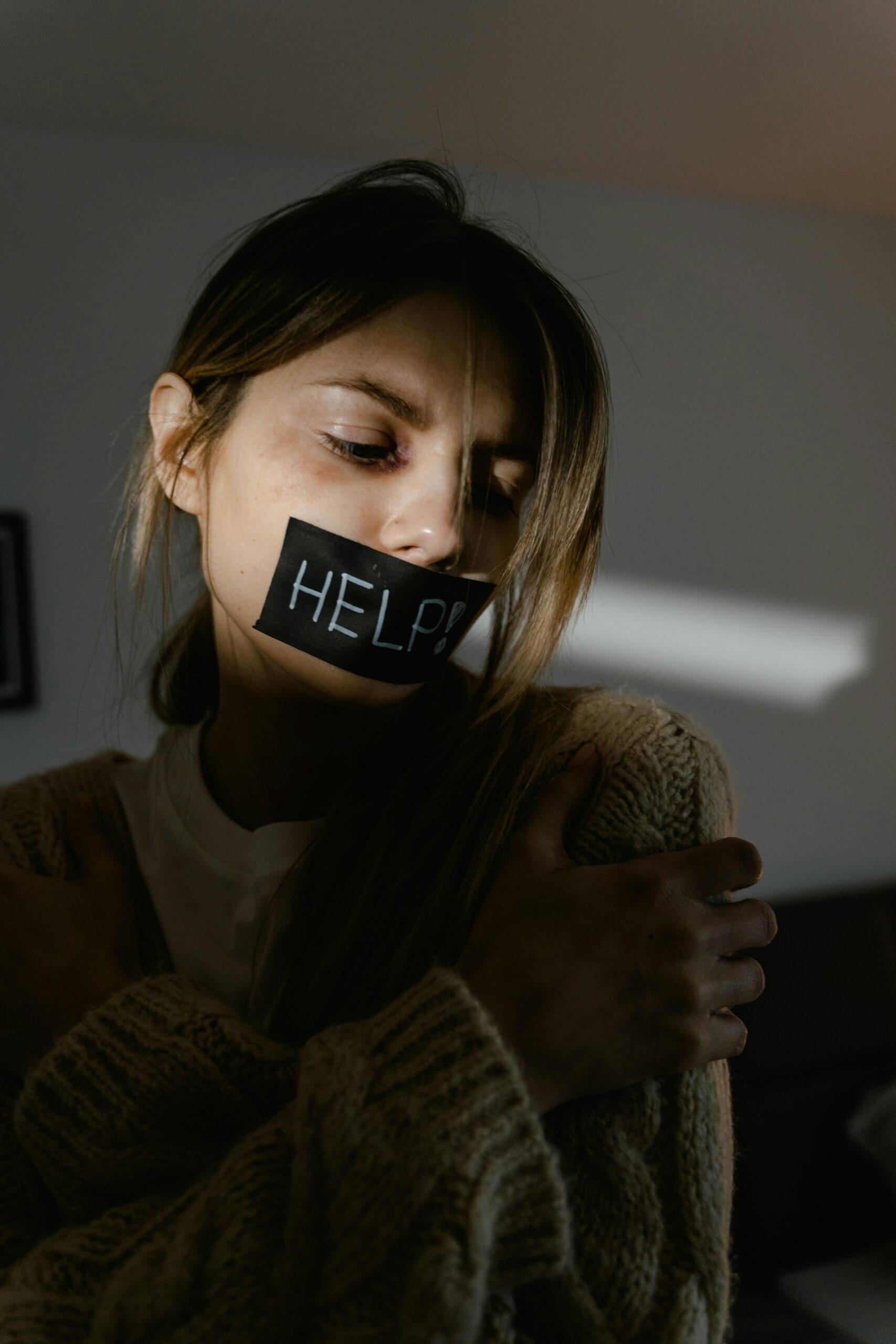 Distressed woman with 'HELP' on mouth in moody lighting, symbolizing silence and pressure.