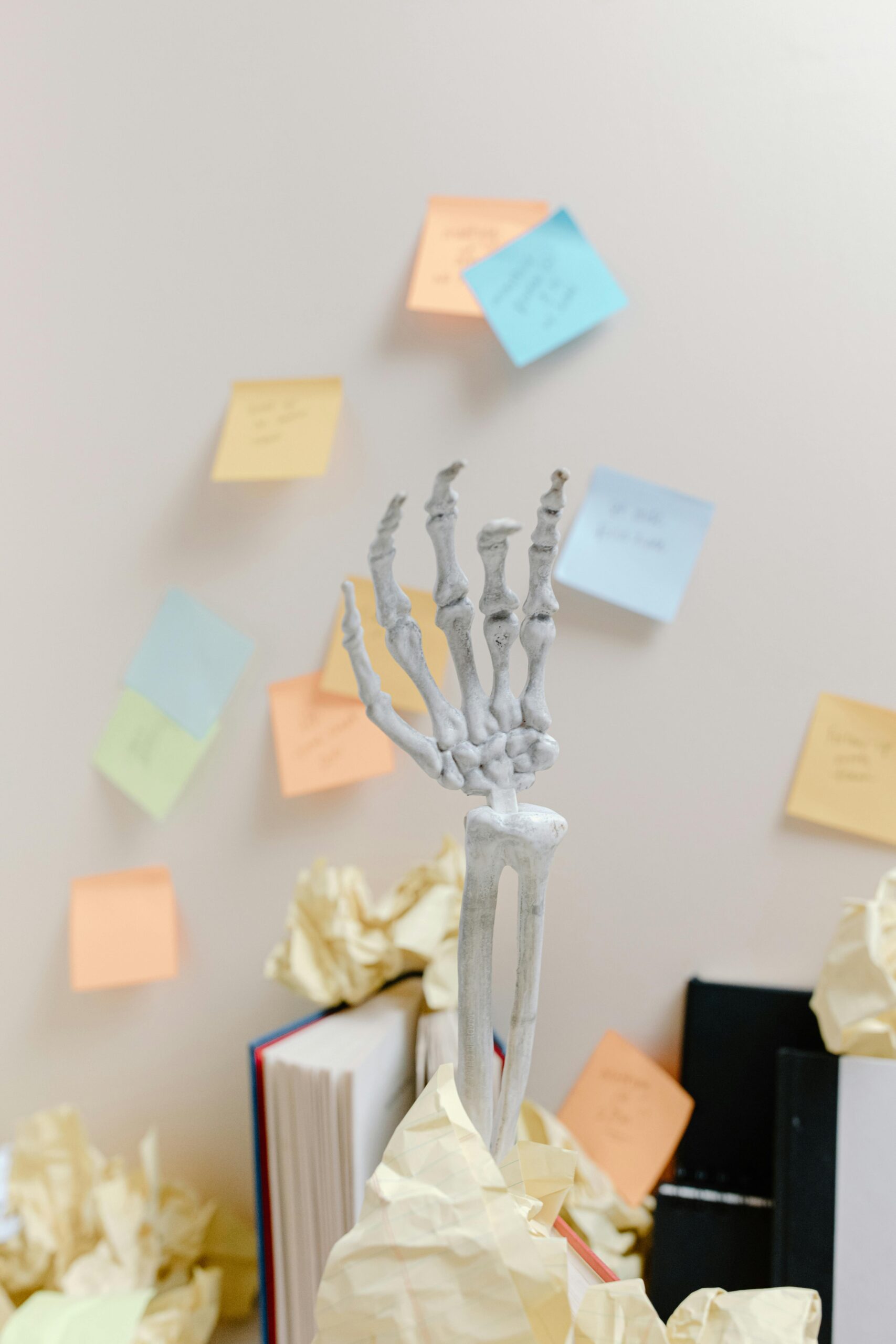 A skeleton hand amongst scattered papers and colorful sticky notes in a cluttered office setting.