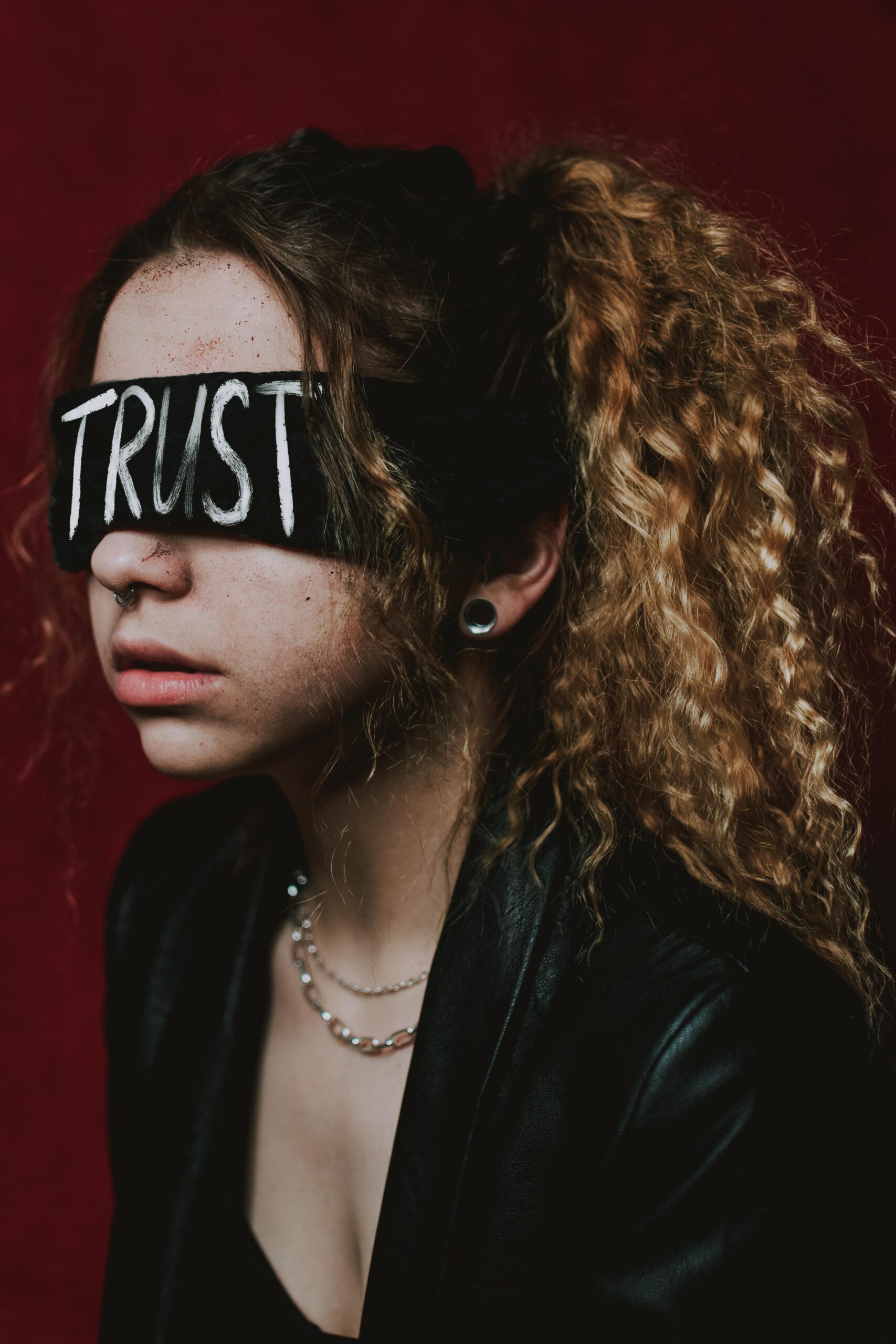 A woman wearing a blindfold with the word 'Trust' against a dark background.